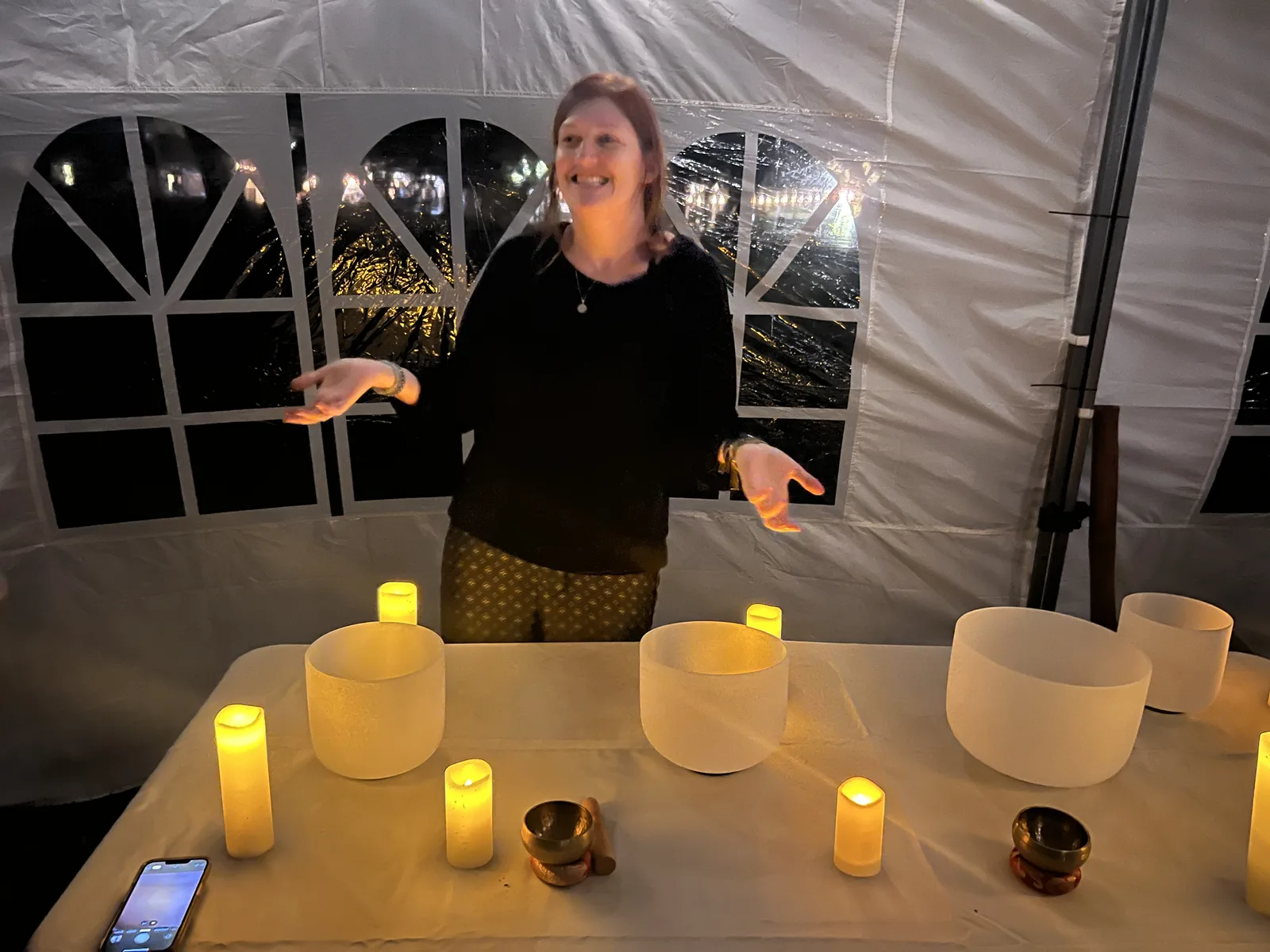 A woman smiling behind the crystal singing bowl table, tent lit up behind her