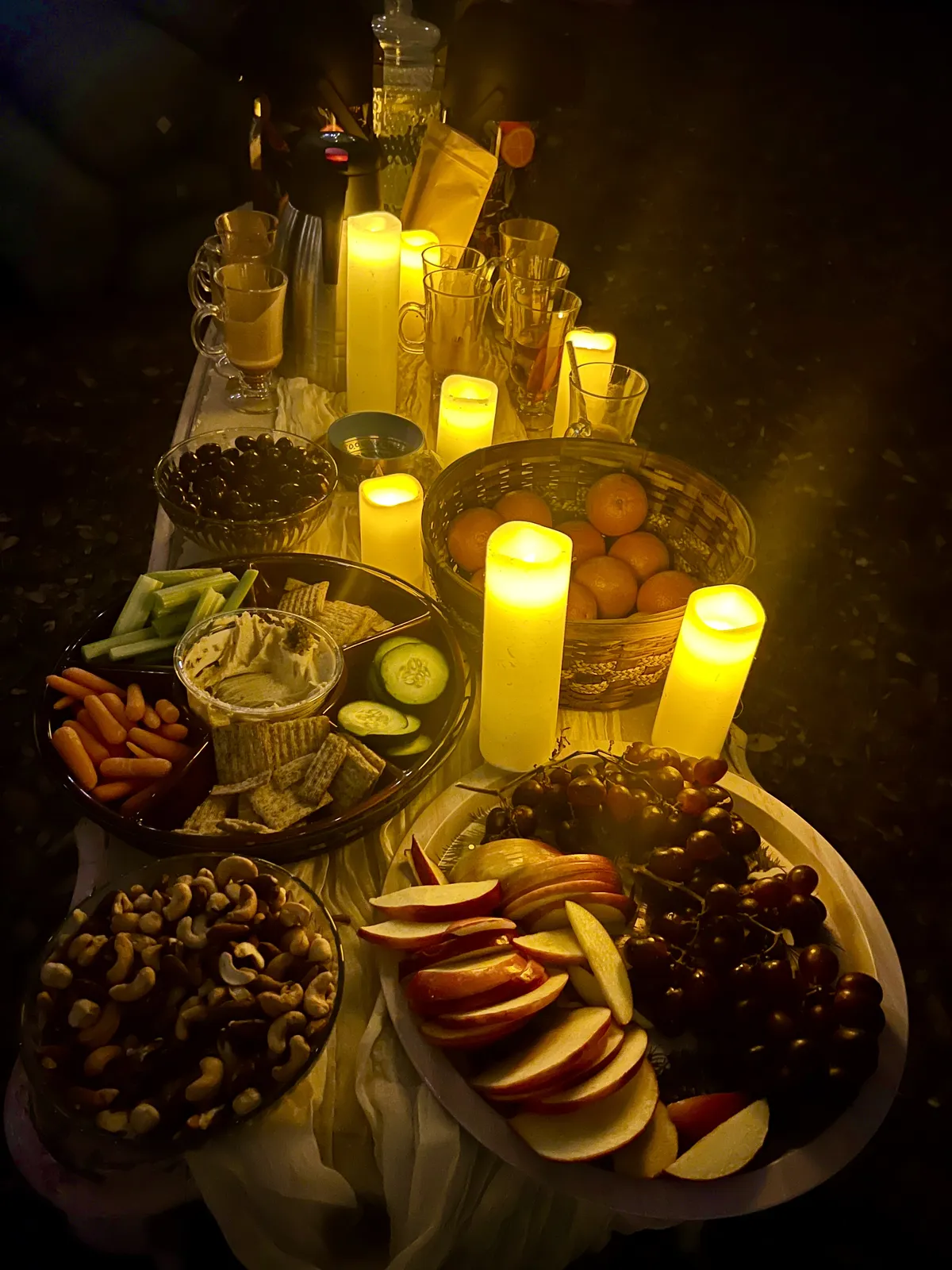Candlelit tea and gathering table set outdoors with fruit and snacks