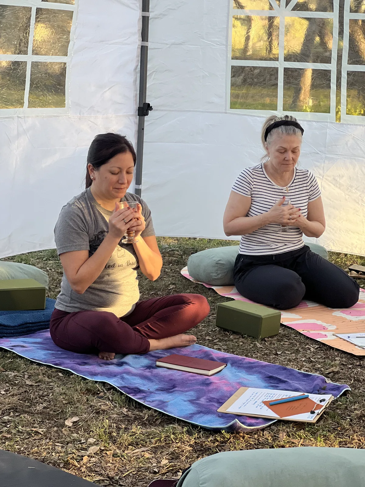 Two women seated on a blanket outdoors, smiling together over reading cards