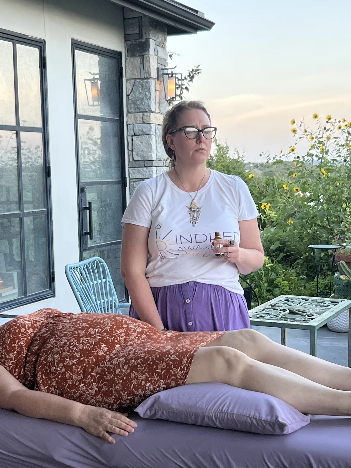 A practitioner leading a bodywork session at sunset, sunflowers in the background