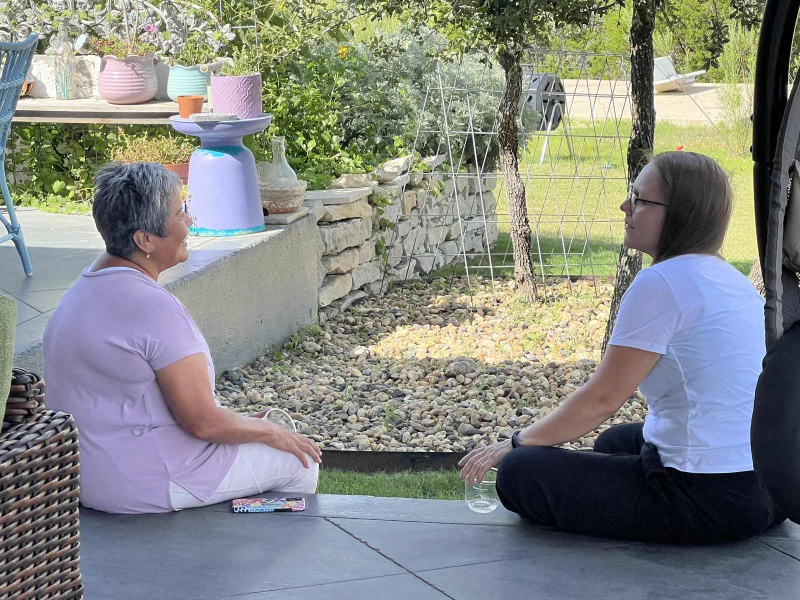 Two women in quiet conversation seated on a garden patio