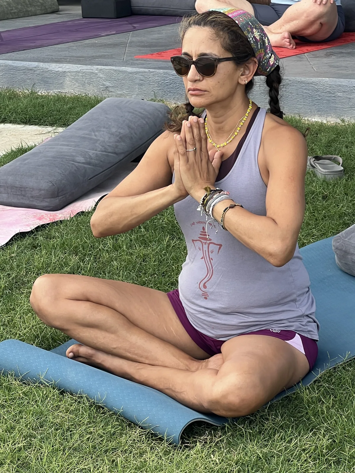 A woman seated in lotus pose with hands together in prayer position, outdoors